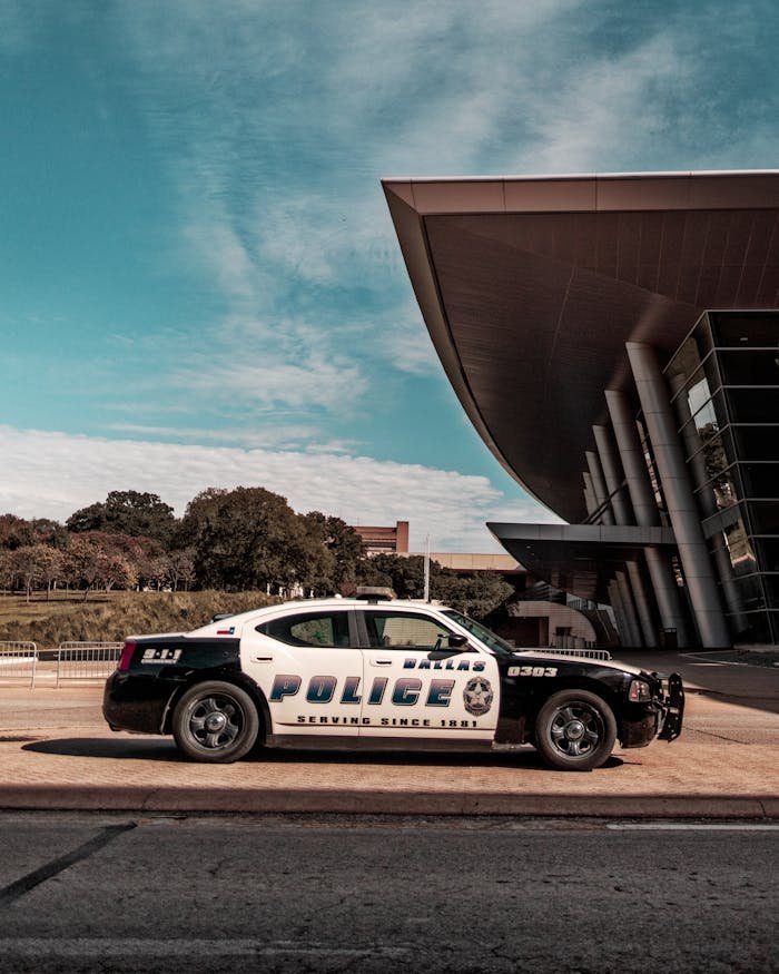 A police car parked outside a modern architectural building during the day with clear blue skies.